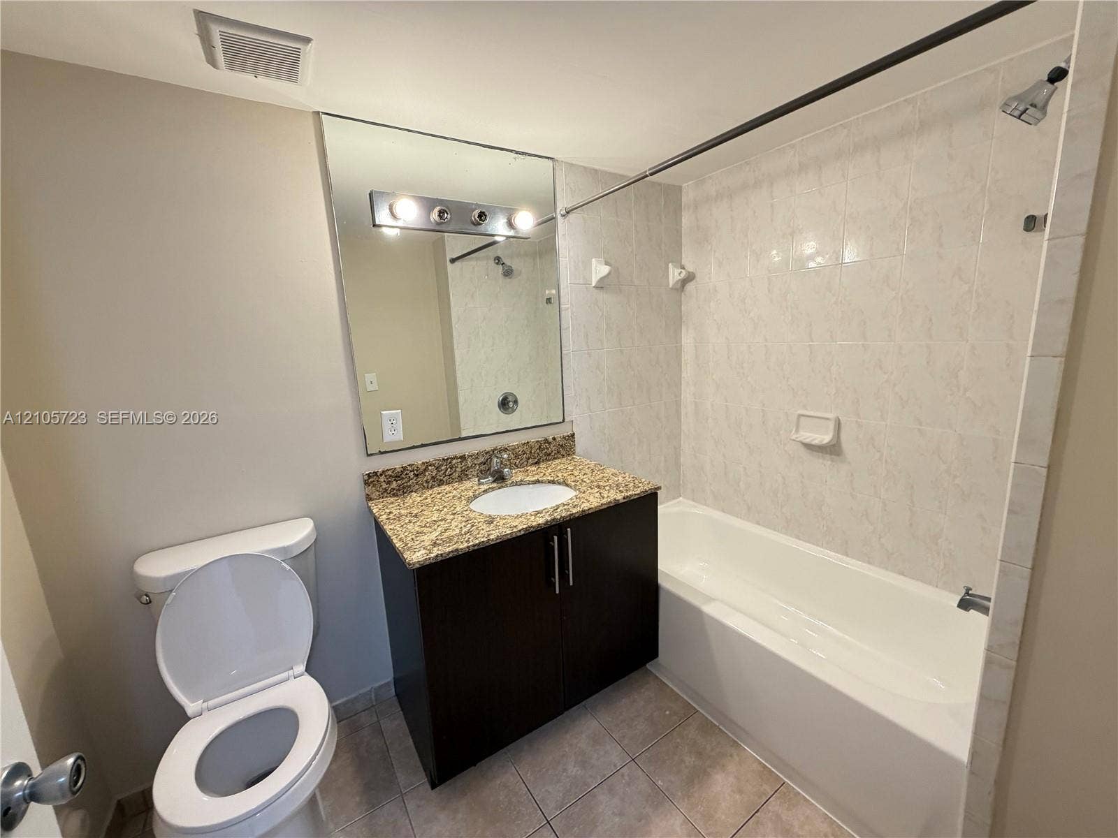 4785 SW 62nd Avenue, #102, Davie, Davie, FL 33314 Bathroom featuring a vanity with dark cabinetry and a stone-finish countertop, undermount sink, wall-mounted mirror, and a tiled shower surround
