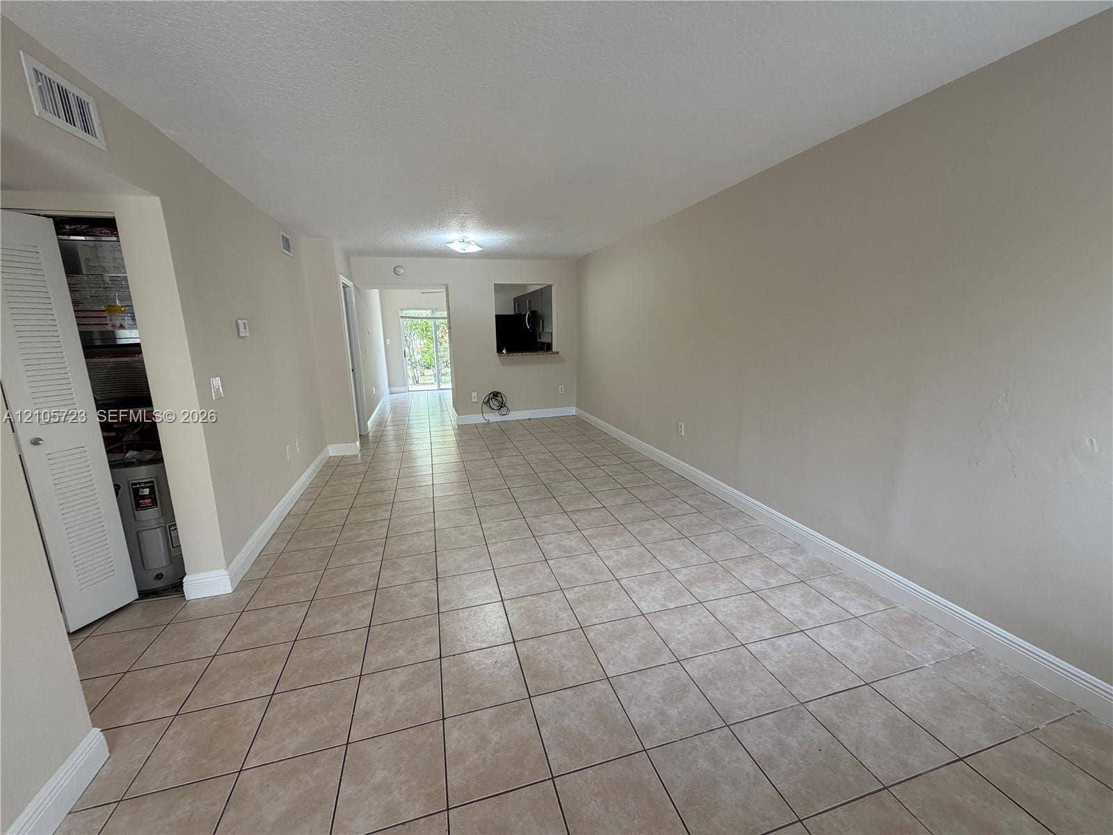 4785 SW 62nd Avenue, #102, Davie, Davie, FL 33314 Open-concept interior featuring neutral-toned walls, tile flooring, a pass-through opening to the kitchen, and a glass sliding door