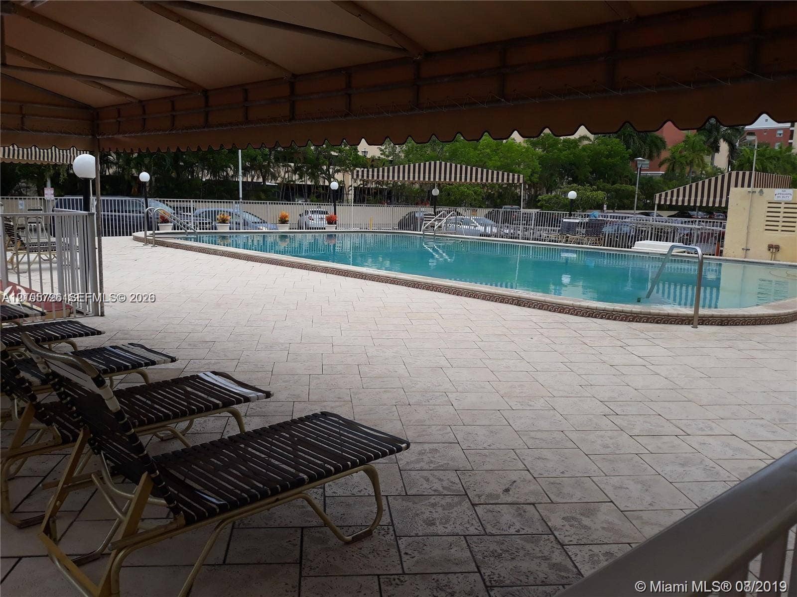 200 172nd Street, #101, Sunny Isles Beach, FL 33160 Swimming pool with paved surround, featuring a shaded canopy area and metal perimeter fencing