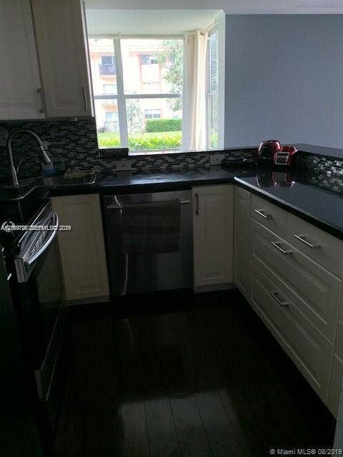 200 172nd Street, #101, Sunny Isles Beach, FL 33160 Kitchen featuring light-toned cabinetry, dark stone countertops, mosaic tile backsplash, stainless steel appliances, and large-format window