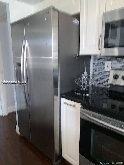200 172nd Street, #101, Sunny Isles Beach, FL 33160 Stainless steel side-by-side refrigerator, white shaker-style cabinetry, dark solid-surface countertop, glass mosaic tile backsplash, and stainless steel built-in microwave