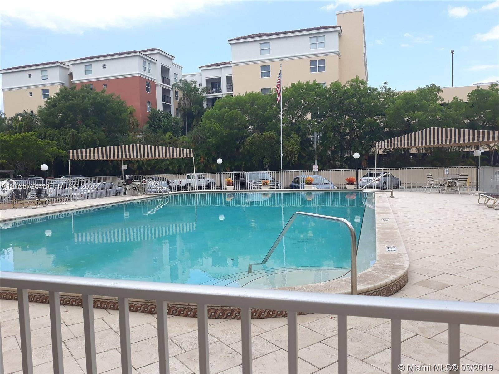200 172nd Street, #101, Sunny Isles Beach, FL 33160 Rectangular swimming pool featuring a tiled deck, metal handrails, and striped architectural awnings