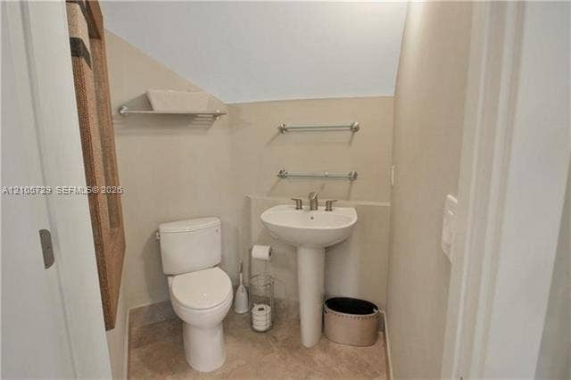 Powder room featuring a white pedestal sink with a chrome faucet, a dual-flush toilet, stone-finish tile flooring, and wall-mounted metal hardware