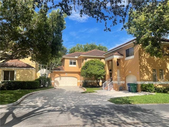 Stucco exterior featuring a multi-car garage, pitched tile roof, arched entryway with white railing, and a concrete driveway