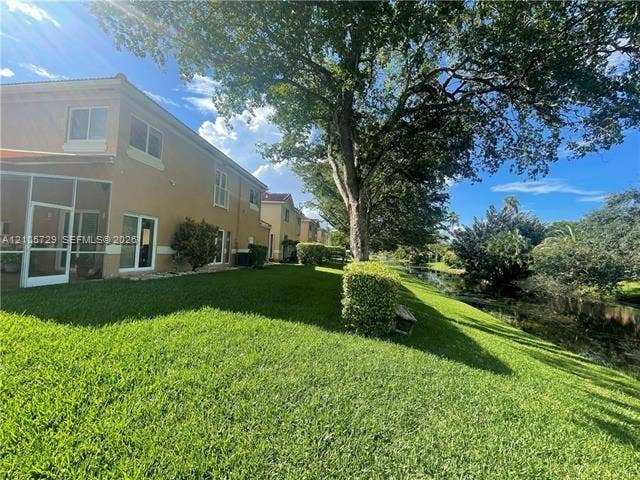 Two-story exterior featuring a screened-in patio, stucco facade, expansive lawn, mature shade trees, and waterfront perimeter