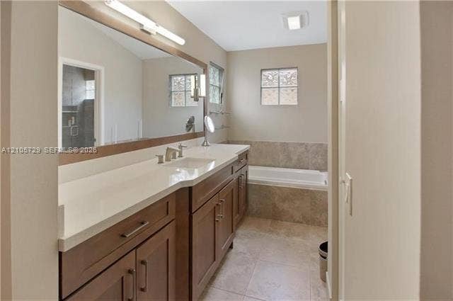 Bathroom featuring a vanity with wood-finish cabinetry, a solid surface countertop, an expansive wall-to-wall mirror, and a tile-surround bathtub
