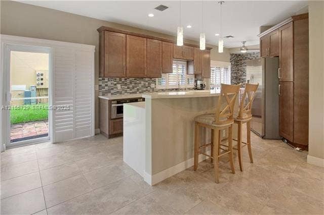 Kitchen featuring wood cabinetry, quartz-topped peninsula, multi-colored stone tile backsplash, large-format tile flooring, and sliding glass door with plantation shutters