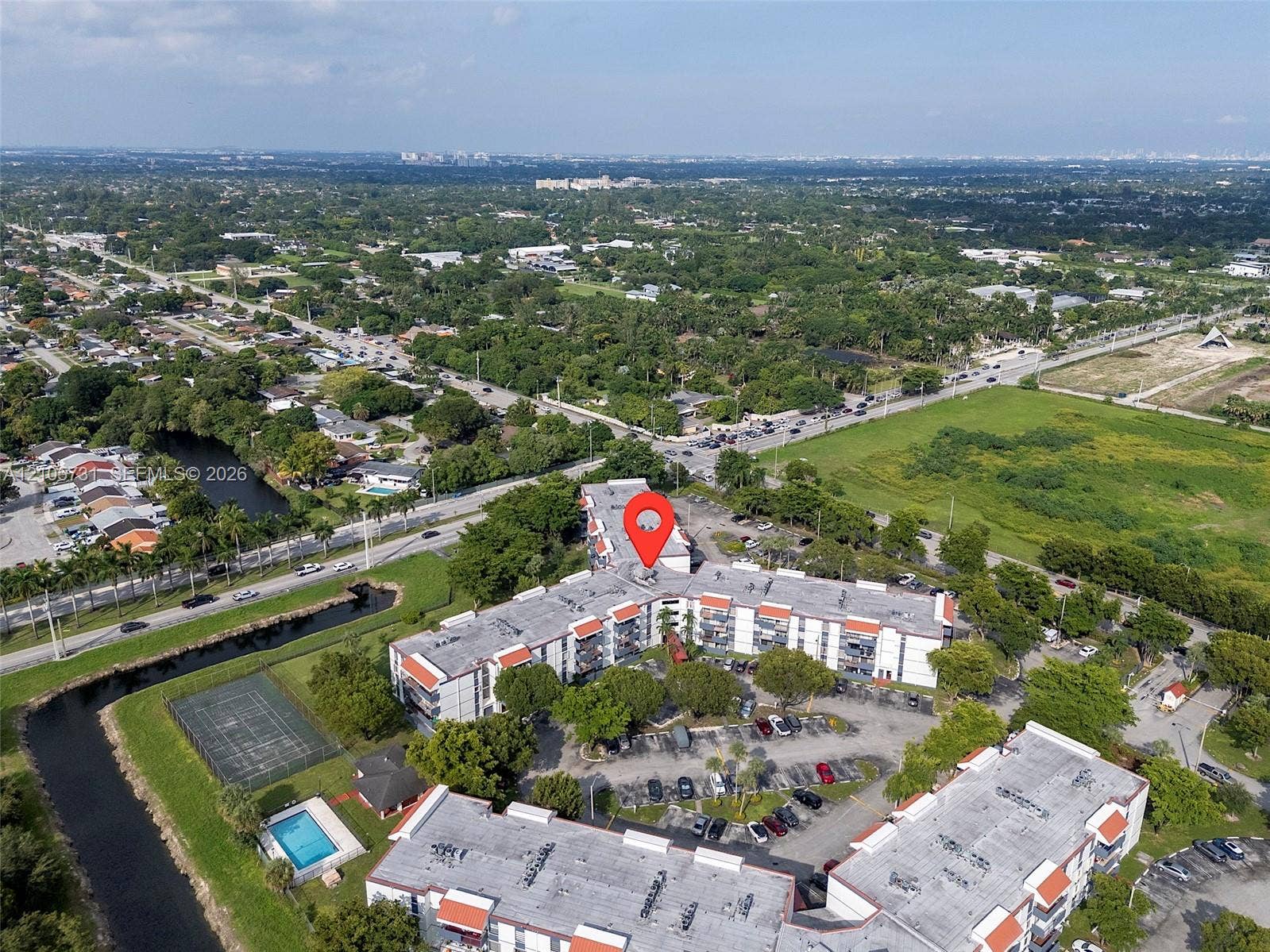 5700 SW 127th Avenue, #1404, Miami, FL 33183 Aerial perspective of a multi-story residential building featuring integrated surface parking, an outdoor swimming pool, and a hardscaped tennis court