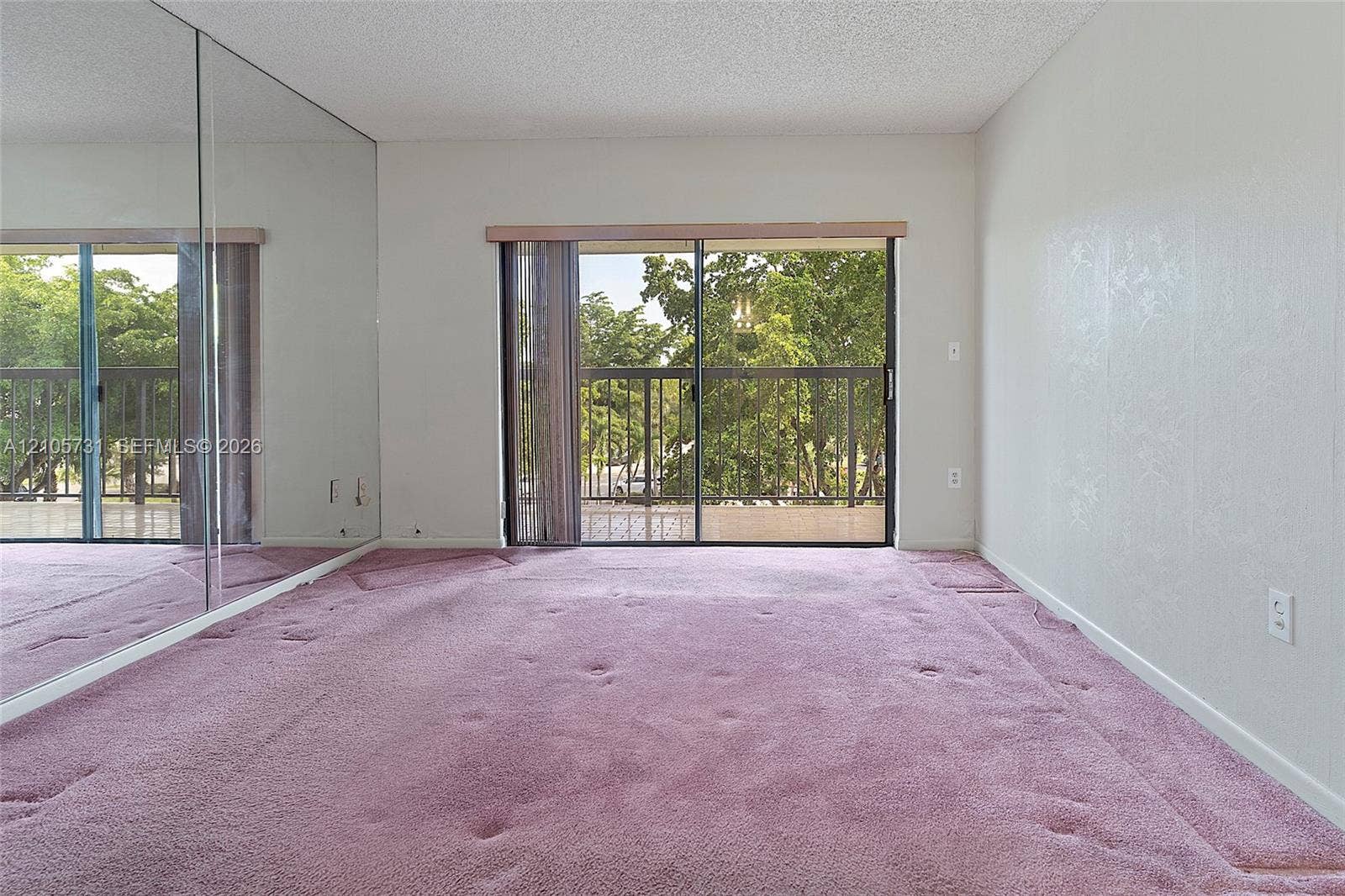5700 SW 127th Avenue, #1404, Miami, FL 33183 Room featuring a wall of floor-to-ceiling mirror panels, carpeted flooring, and a sliding glass door providing external access to a balcony with metal railings