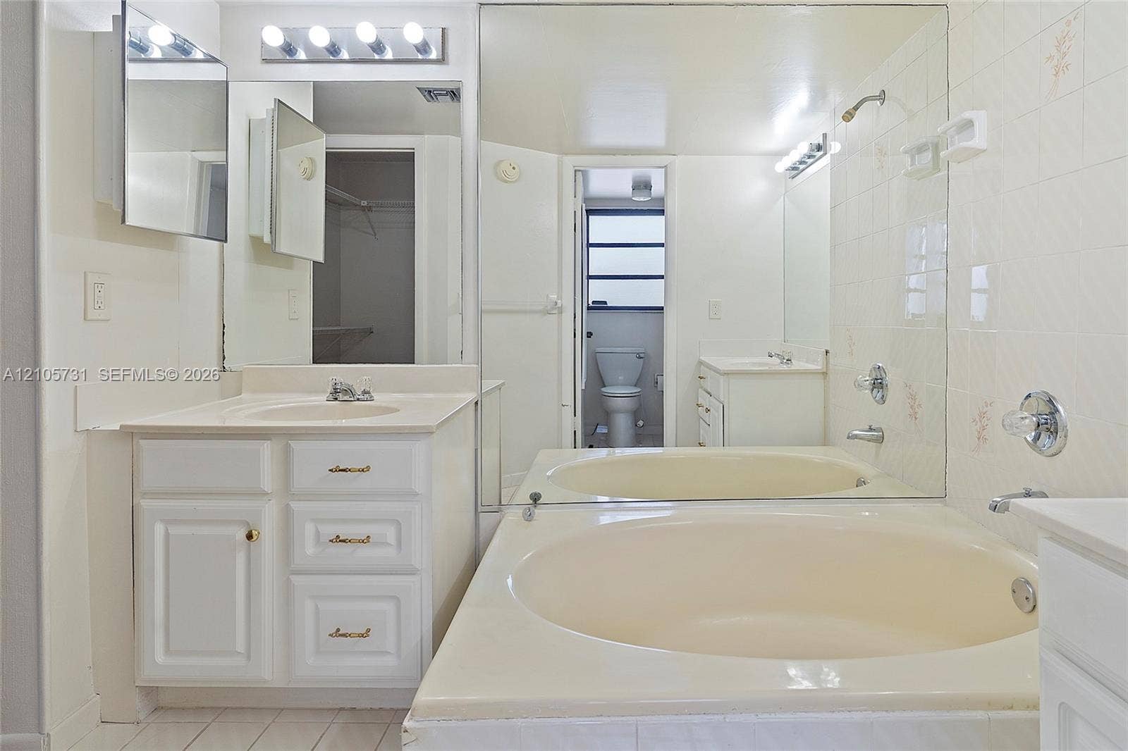 5700 SW 127th Avenue, #1404, Miami, FL 33183 Bathroom featuring an oval soaking tub with a tiled surround, a white cabinetry vanity, an expansive wall-mounted mirror, and multi-bulb vanity lighting