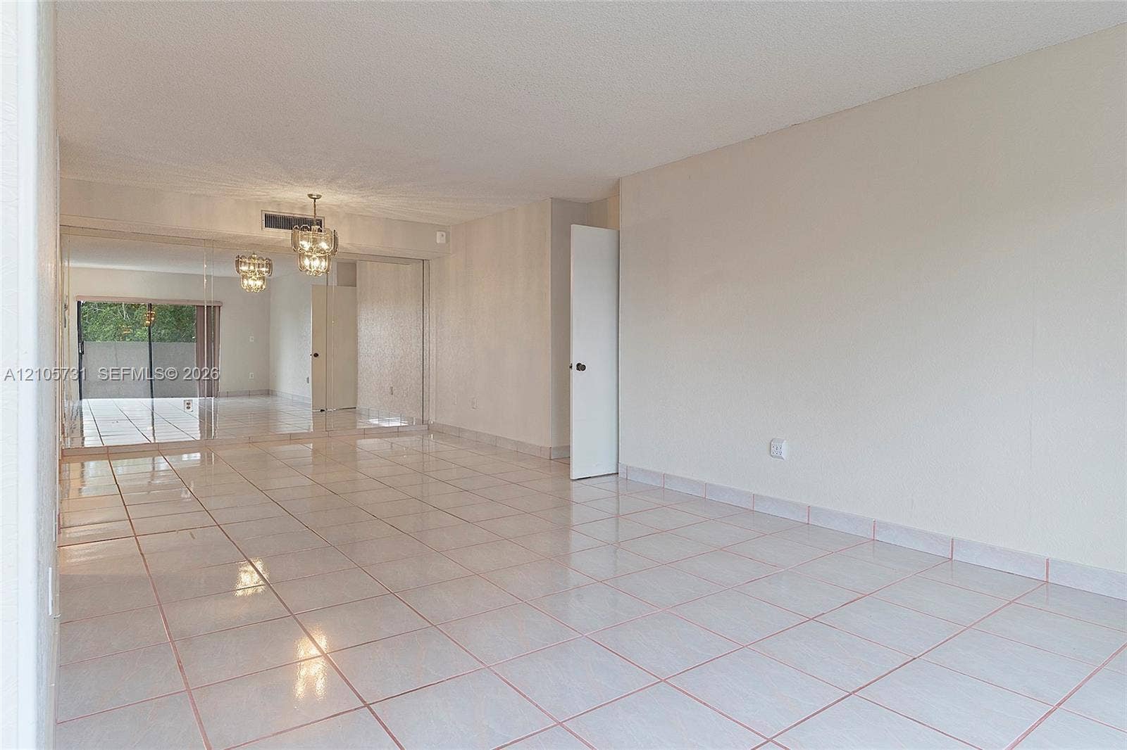 5700 SW 127th Avenue, #1404, Miami, FL 33183 Neutral-toned interior space featuring light-colored ceramic tile flooring, mirrored wall panels, and a central crystal-style chandelier