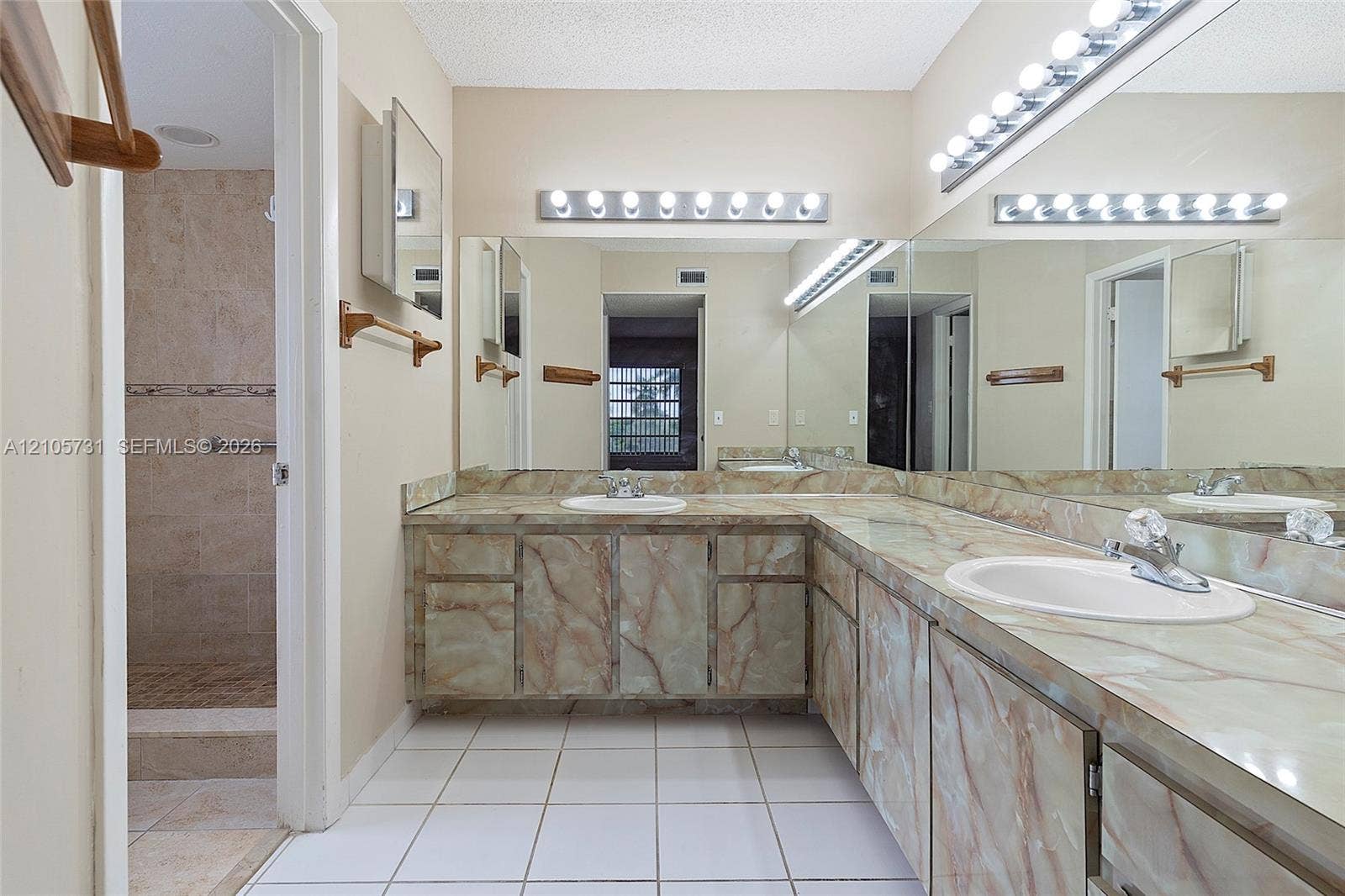 5700 SW 127th Avenue, #1404, Miami, FL 33183 L-shaped vanity featuring custom-fitted stone-finish cabinetry and countertops, dual white drop-in sinks, extensive full-width wall mirrors, and integrated multi-bulb lighting fixtures
