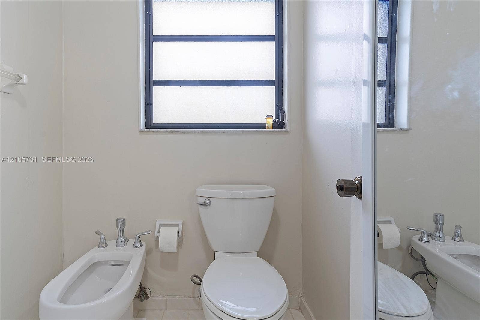 5700 SW 127th Avenue, #1404, Miami, FL 33183 White ceramic toilet, bidet with chrome faucet hardware, and horizontal-pane window with dark frame