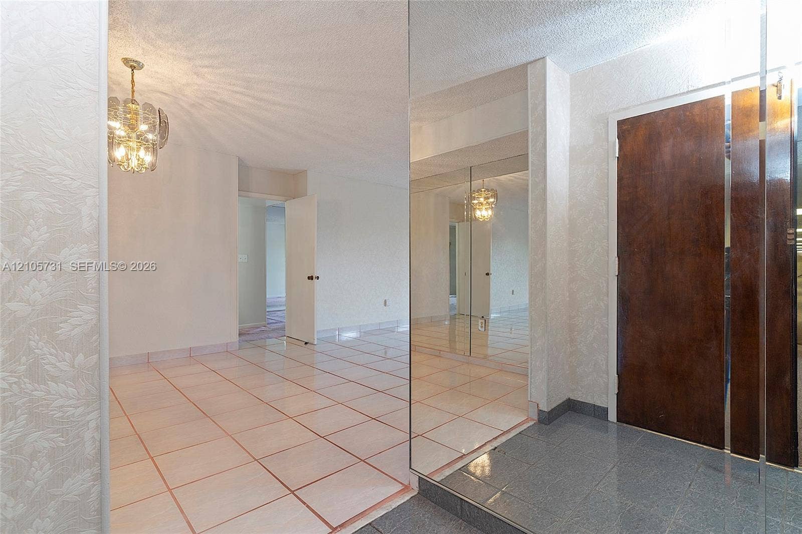 5700 SW 127th Avenue, #1404, Miami, FL 33183 Entryway featuring a stone-tile floor, floor-to-ceiling mirrored wall panels, decorative multi-tiered pendant lighting, and a solid wood door with brushed metal trim