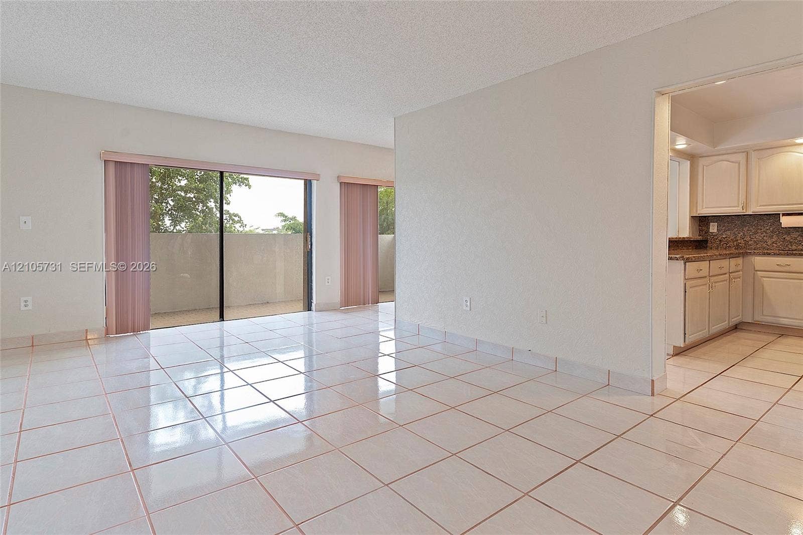 5700 SW 127th Avenue, #1404, Miami, FL 33183 Open-concept interior featuring light-toned tile flooring, sliding glass doors, and kitchen cabinetry with integrated stone-surface countertops