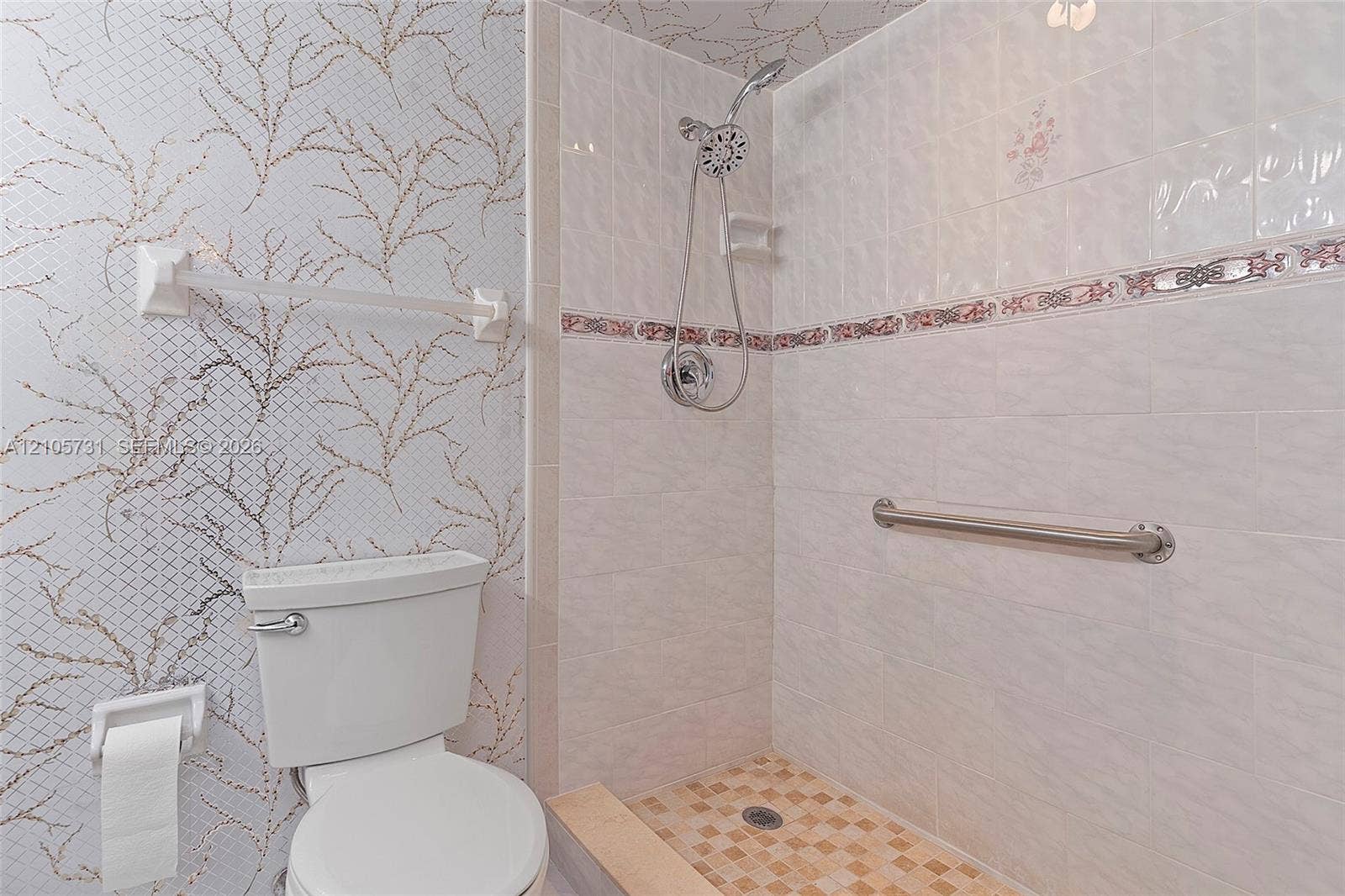 5700 SW 127th Avenue, #1404, Miami, FL 33183 Bathroom featuring a tiled walk-in shower with chrome hand-held showerhead, integrated metallic accent tile border, chrome grab bar, and patterned wall covering