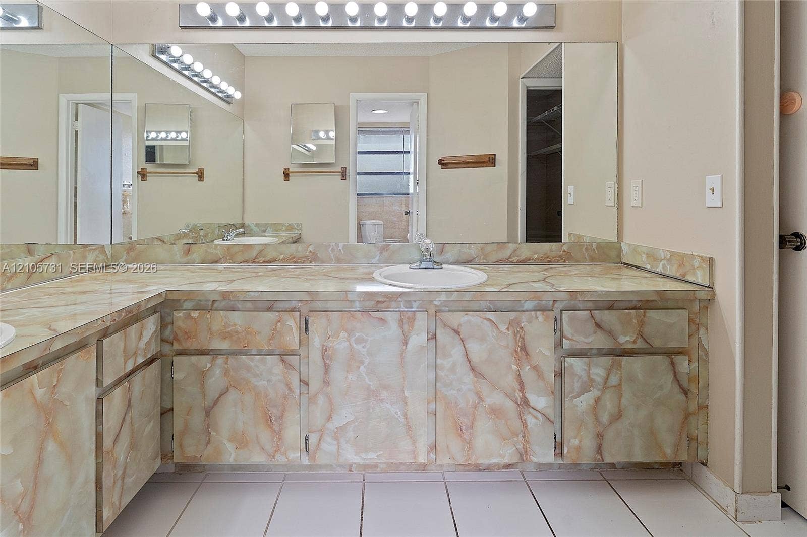 5700 SW 127th Avenue, #1404, Miami, FL 33183 Double vanity featuring natural stone-patterned cabinetry and matching stone countertop with drop-in sinks, wall-to-wall mirror, and overhead multi-bulb lighting