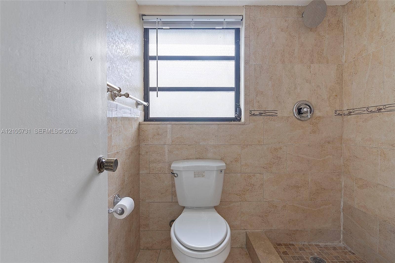 5700 SW 127th Avenue, #1404, Miami, FL 33183 Bathroom featuring full-height neutral stone-finish tile wall surround, stone-tiled shower floor, recessed window with a shutter, chrome plumbing fixtures, and a wall-mounted metal towel bar
