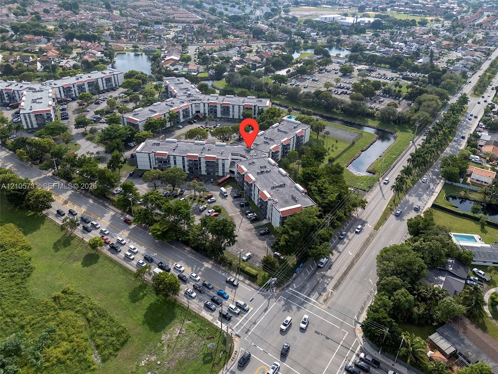5700 SW 127th Avenue, #1404, Miami, FL 33183 Aerial perspective of a multi-story residential building featuring asphalt roofing, exterior balconies, surface parking, and surrounding landscape areas