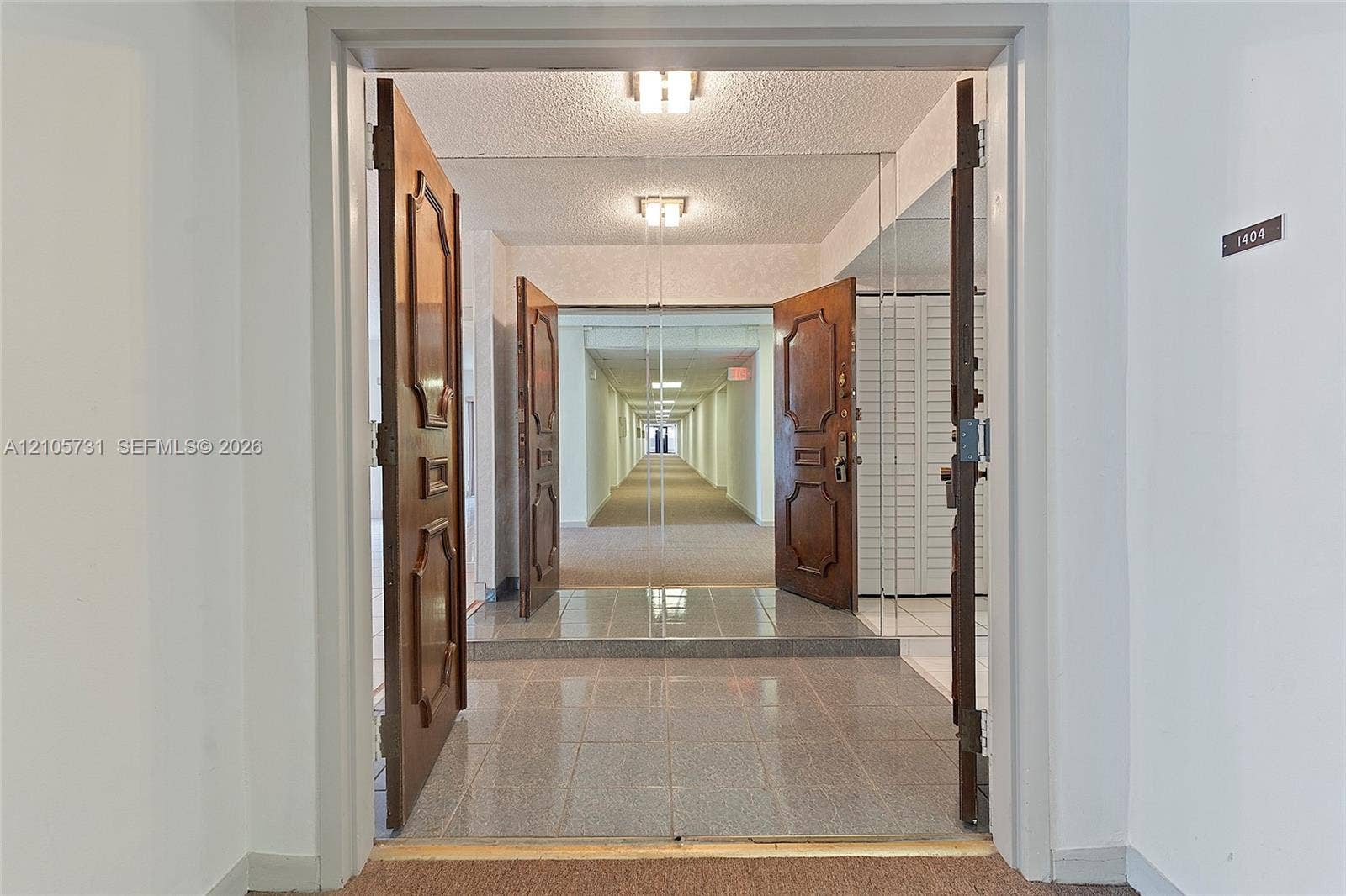 5700 SW 127th Avenue, #1404, Miami, FL 33183 Entryway featuring double solid-wood doors with decorative panels, polished stone-finish floor tiling, and integrated wall-to-wall mirror paneling