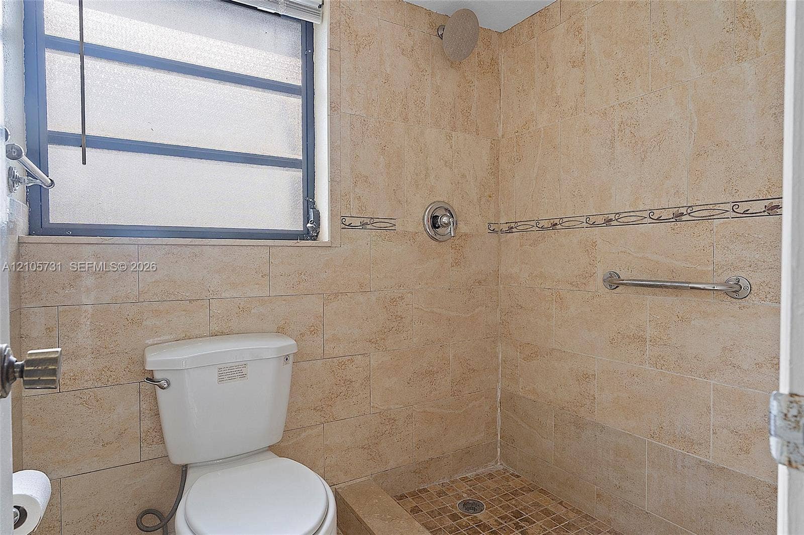 5700 SW 127th Avenue, #1404, Miami, FL 33183 Full-height stone-tile wall finishes, walk-in shower with stone floor tiling, wall-mounted metal grab bar, overhead shower fixture with integrated temperature control, and opaque-glass window