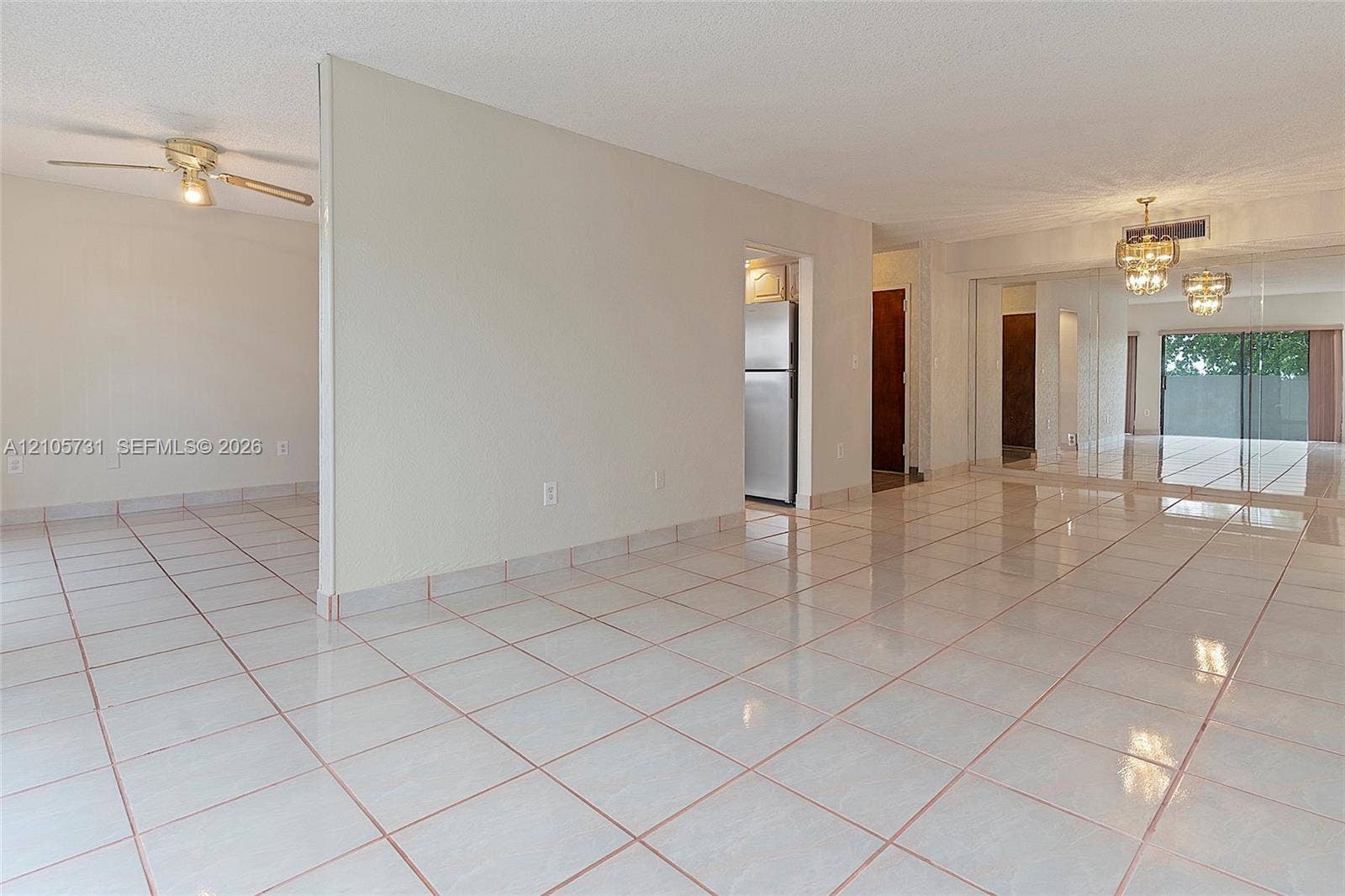 5700 SW 127th Avenue, #1404, Miami, FL 33183 Open-concept interior featuring light-toned tile flooring, mirrored sliding closet doors, a dual-arm ceiling fan, and ornate overhead lighting fixtures