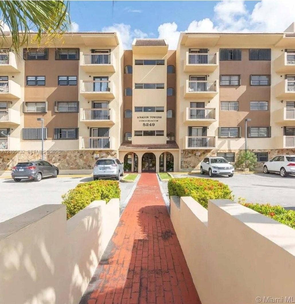 5249 NW 7th Street, #219, Miami, Miami, FL 33126 Multi-story condominium exterior featuring a stone-clad facade, private balconies, an arched entryway, and a paved brick walkway