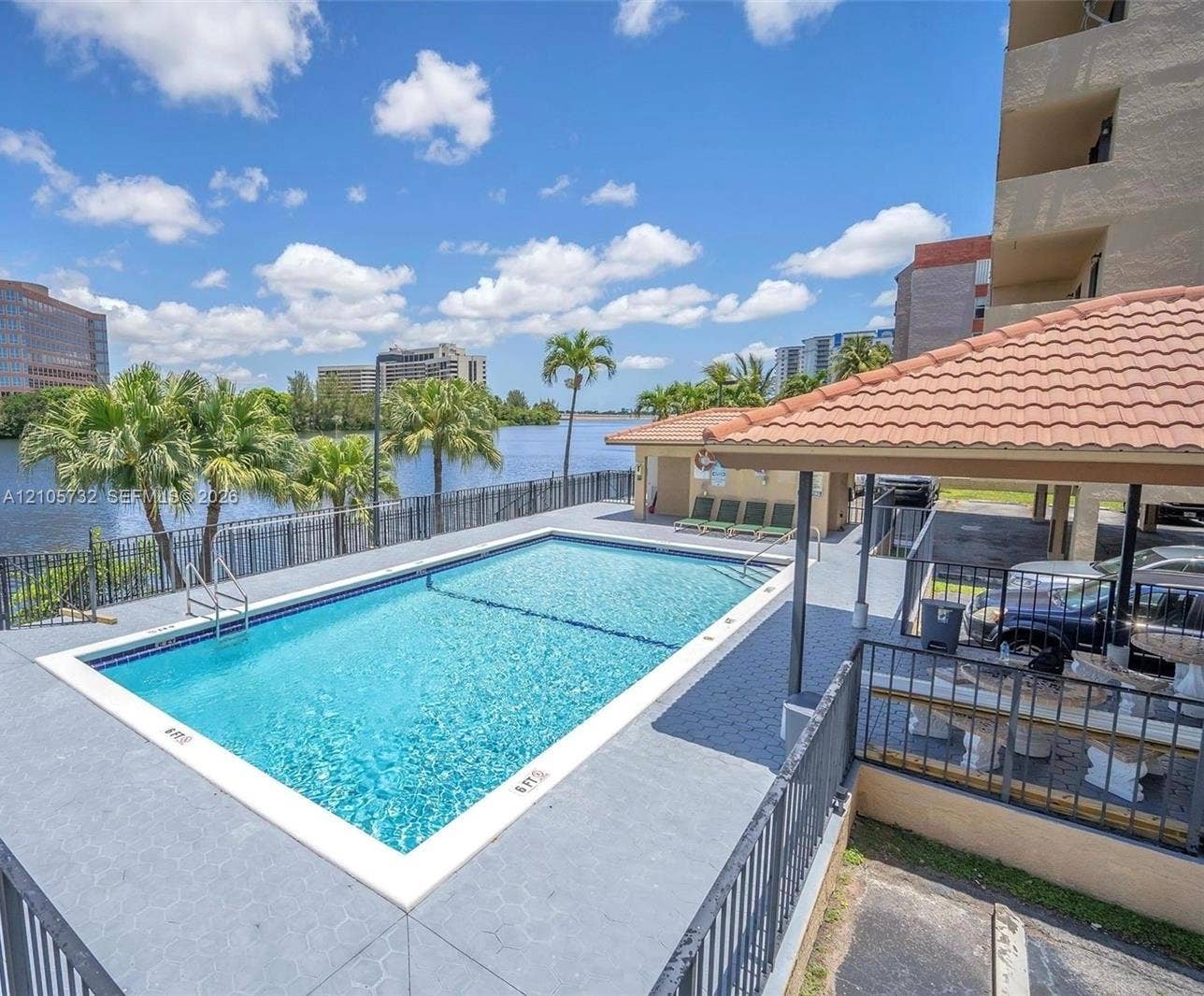 5249 NW 7th Street, #219, Miami, Miami, FL 33126 In-ground swimming pool with a concrete deck, covered pavilion featuring a tiled roof, metal perimeter fencing, and water frontage