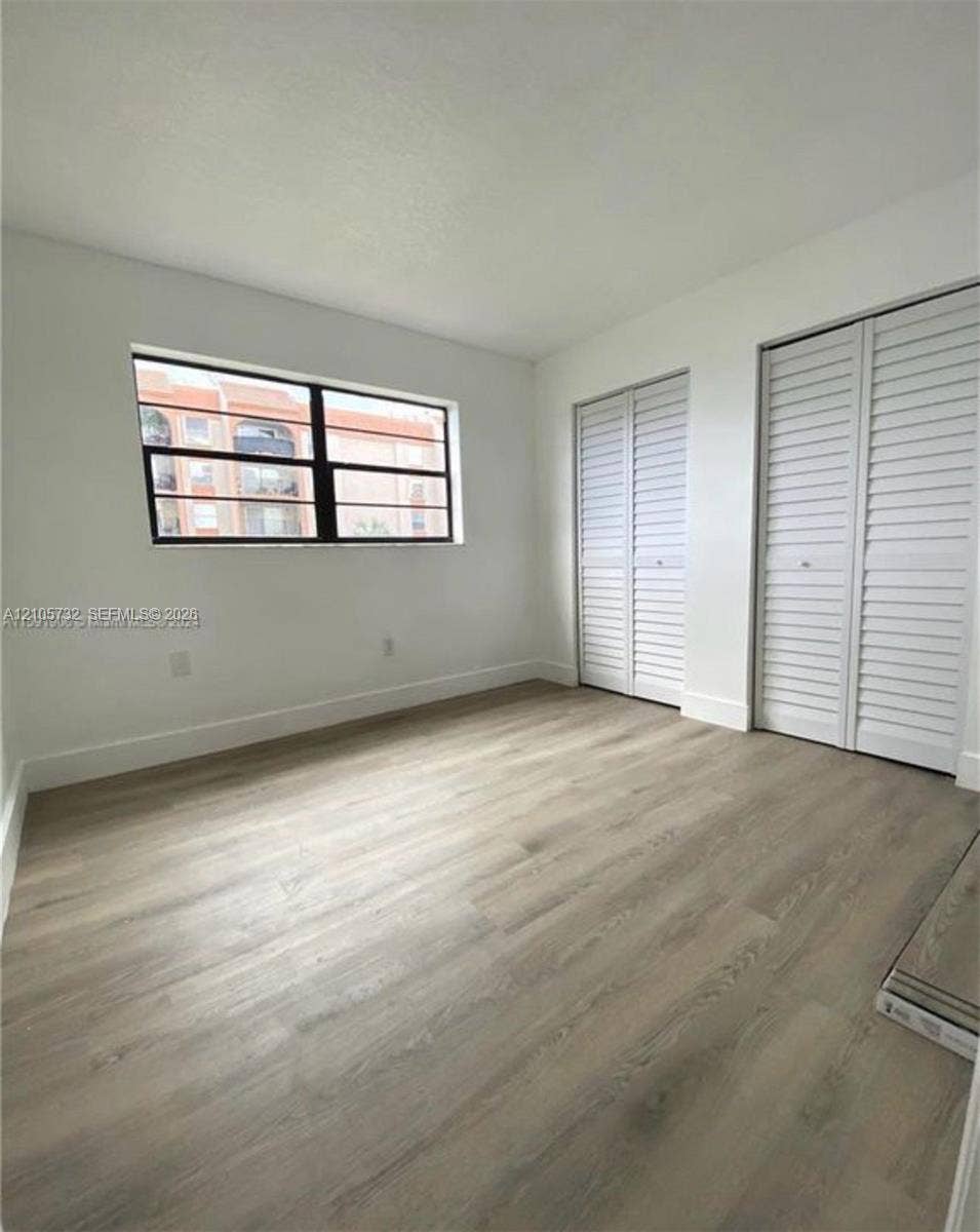 5249 NW 7th Street, #219, Miami, Miami, FL 33126 Wood-finish flooring, two sets of white louvered-style closet doors, and a large horizontal window with a black frame