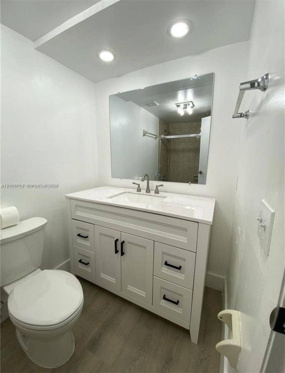5249 NW 7th Street, #219, Miami, Miami, FL 33126 White vanity featuring shaker-style cabinetry, matte black hardware, integrated sink, and stone-surface countertop, complemented by wood-finish flooring and a wall-mounted mirror