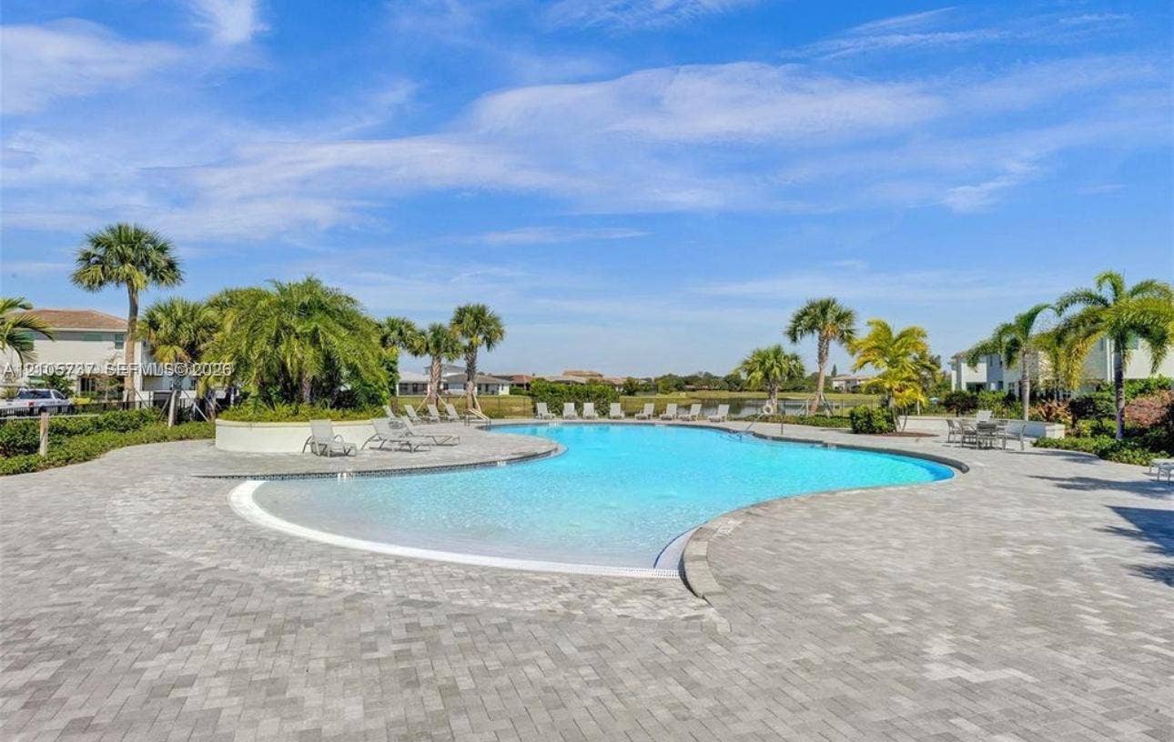 Curvilinear swimming pool with a zero-entry edge, surrounded by expansive stone paver decking and integrated palm tree landscaping