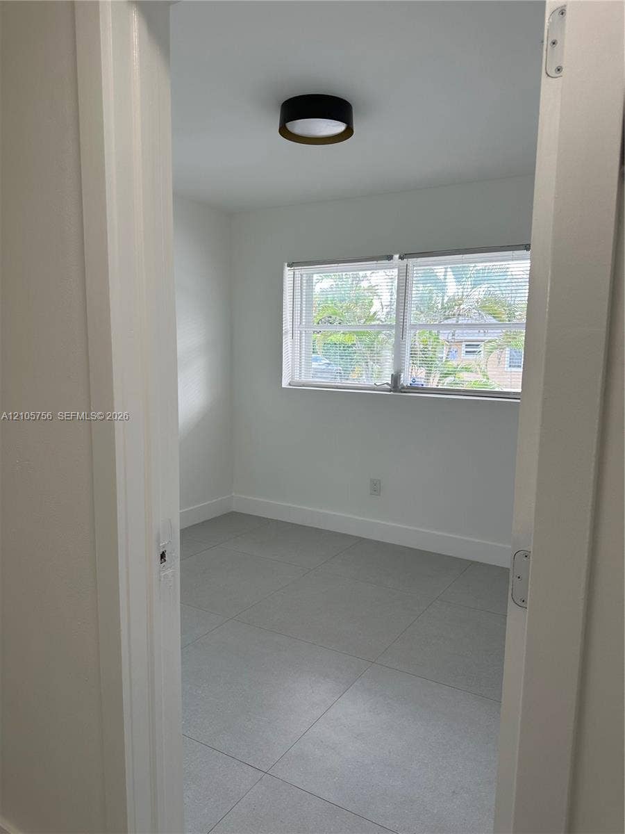 137 SE 2nd Avenue, #A, Hallandale Beach, Hallandale Beach, FL 33009 Neutral-toned interior room featuring large-format ceramic tile flooring, a dual-pane window, and a modern circular flush-mount ceiling light fixture