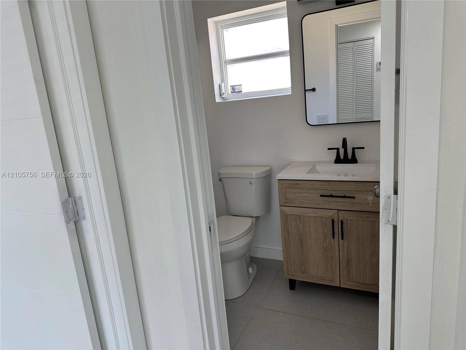 137 SE 2nd Avenue, #A, Hallandale Beach, Hallandale Beach, FL 33009 Bathroom featuring a vanity with a light wood-finish cabinet, stone-composite countertop, matte black fixtures, and a rectangular mirror with a rounded black frame