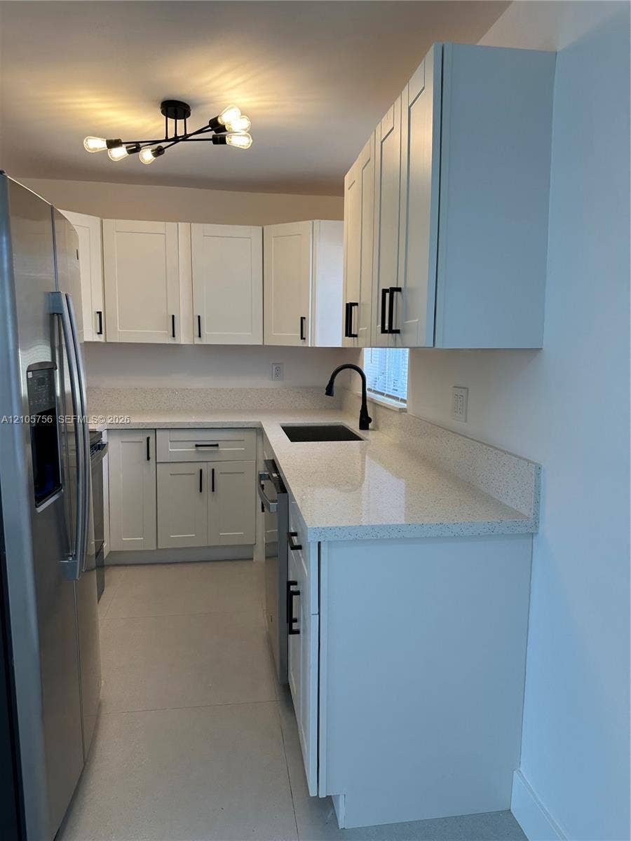 137 SE 2nd Avenue, #A, Hallandale Beach, Hallandale Beach, FL 33009 White cabinetry with black hardware, stone-composite countertops, matte black faucet, integrated stainless steel refrigerator, and multi-bulb architectural ceiling fixture