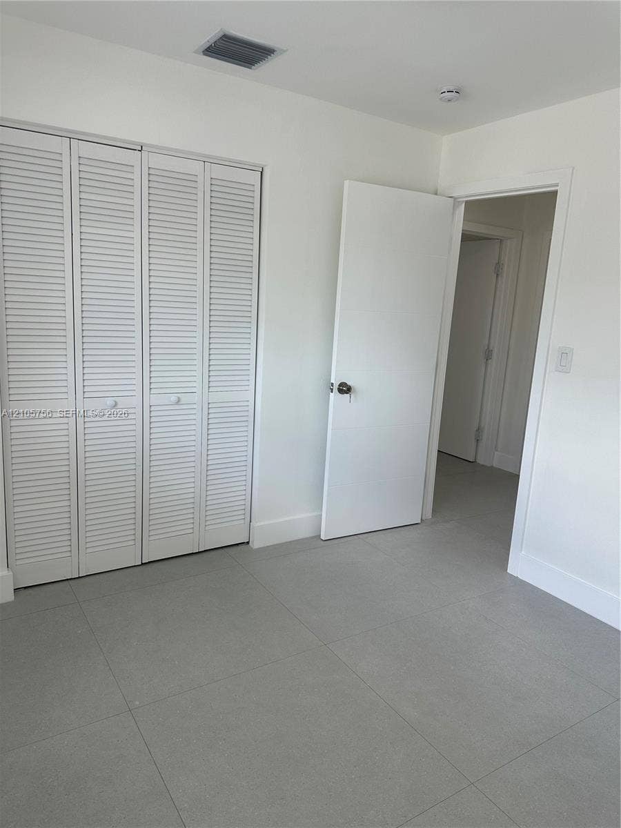 137 SE 2nd Avenue, #A, Hallandale Beach, Hallandale Beach, FL 33009 Neutral-toned large-format tile flooring, white louvered-style bi-fold closet doors, and a solid-core interior swing door with brushed metal hardware