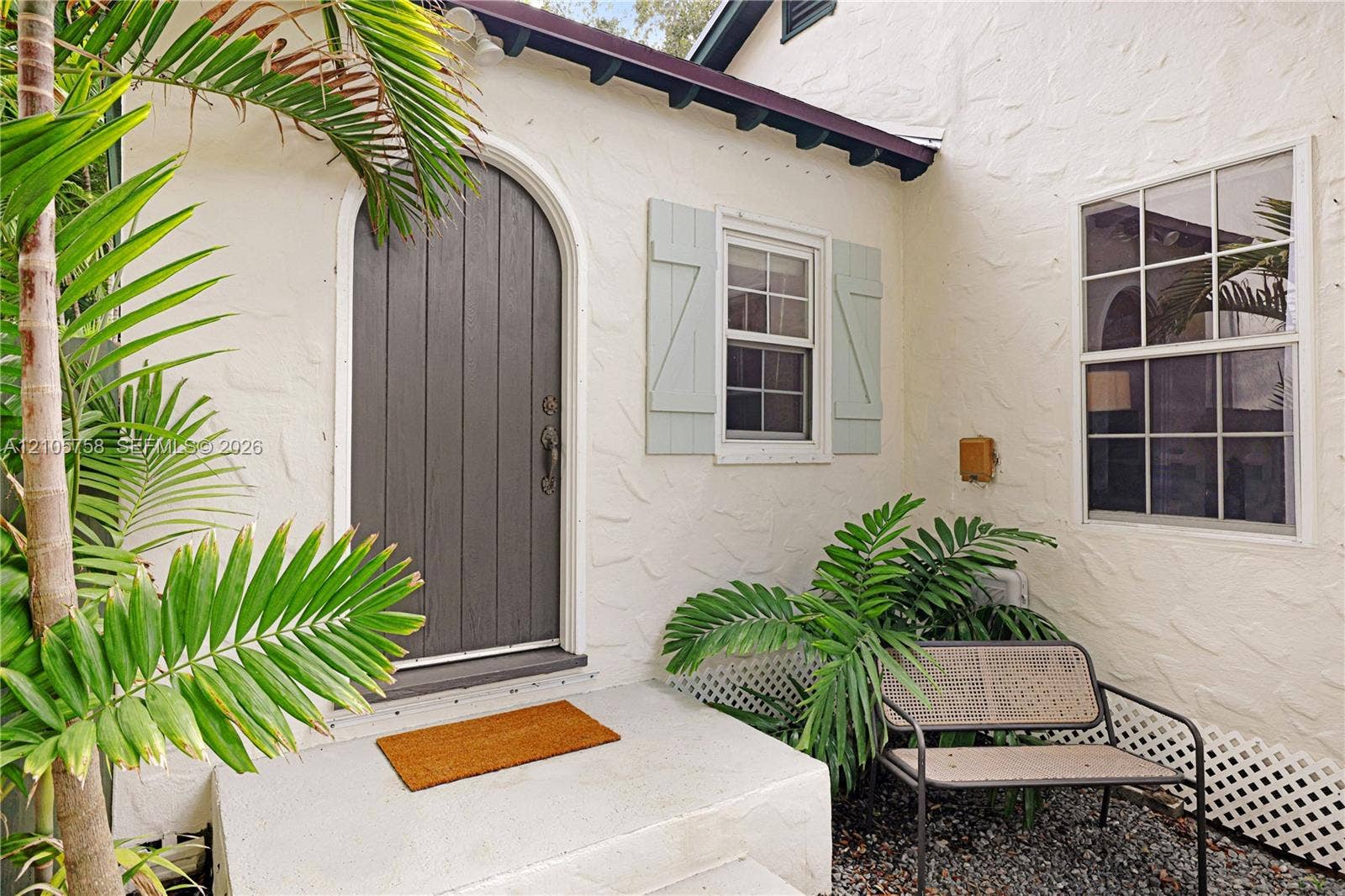668 NE 70th Street, Miami, FL 33138 Textured stucco exterior featuring an arched entry door, paneled window shutters, and a concrete stoop