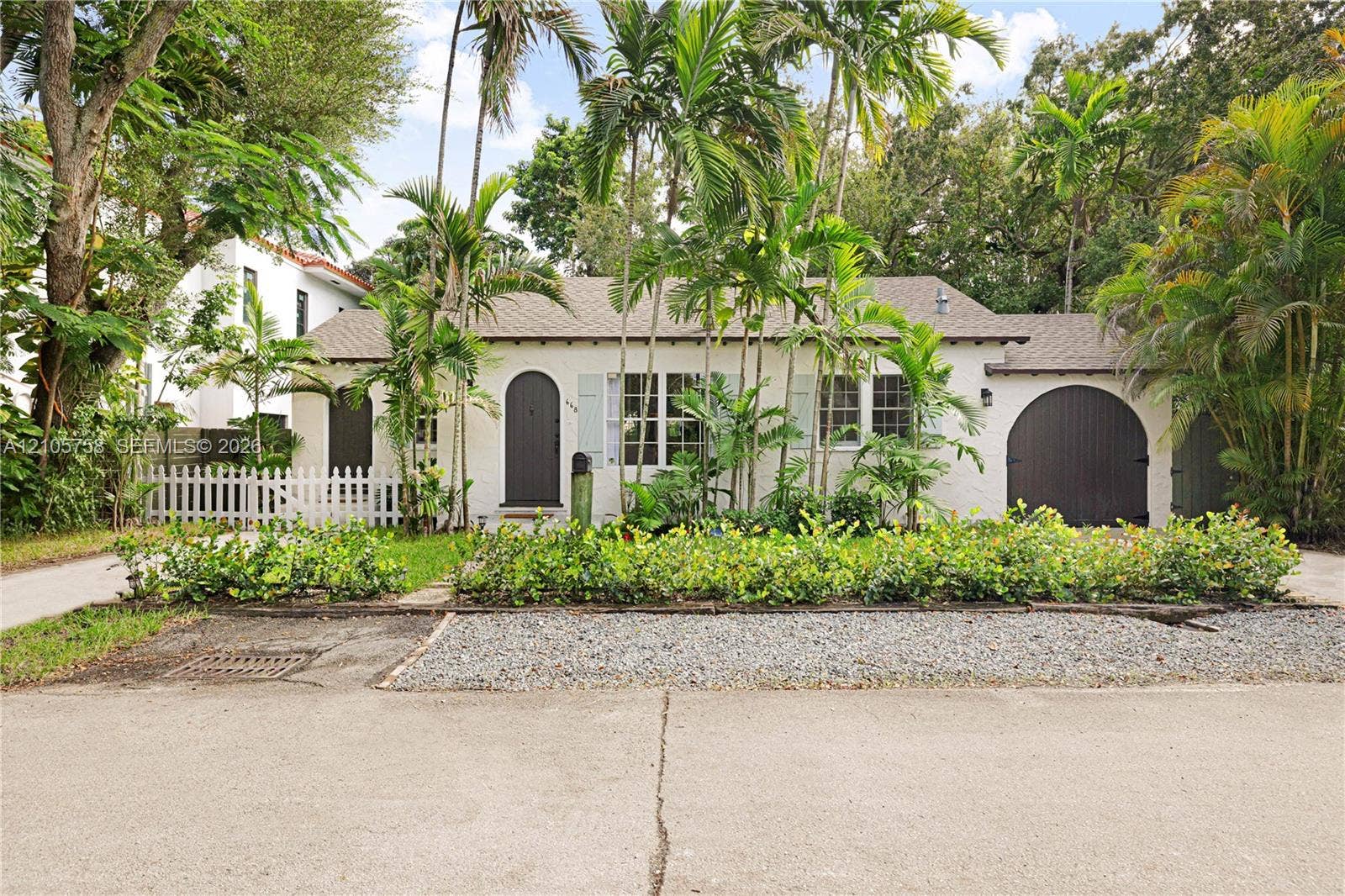 668 NE 70th Street, Miami, FL 33138 Stucco exterior featuring an arched entryway, arched garage door, shuttered windows, and a white picket fence