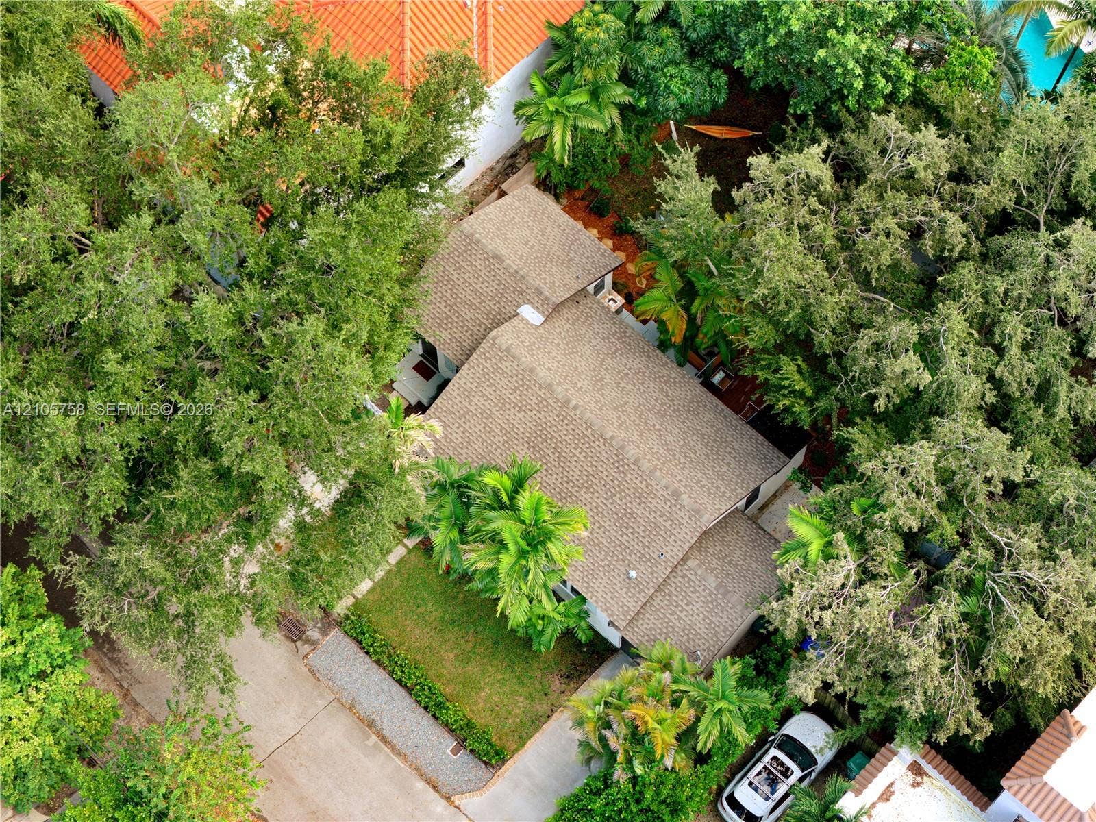 668 NE 70th Street, Miami, FL 33138 Aerial perspective featuring a multi-pitched roof with textured shingles, mature perimeter trees, manicured lawn, and stone-paver walkway