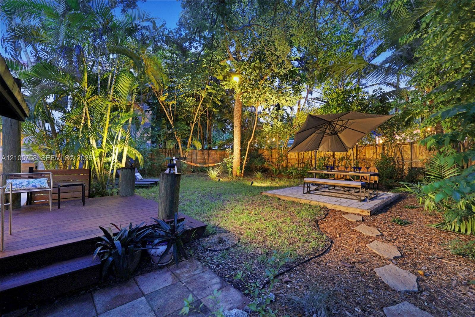 668 NE 70th Street, Miami, FL 33138 Backyard featuring a raised wood-finish deck, paved patio area, stone paver path, mature trees, and privacy fencing