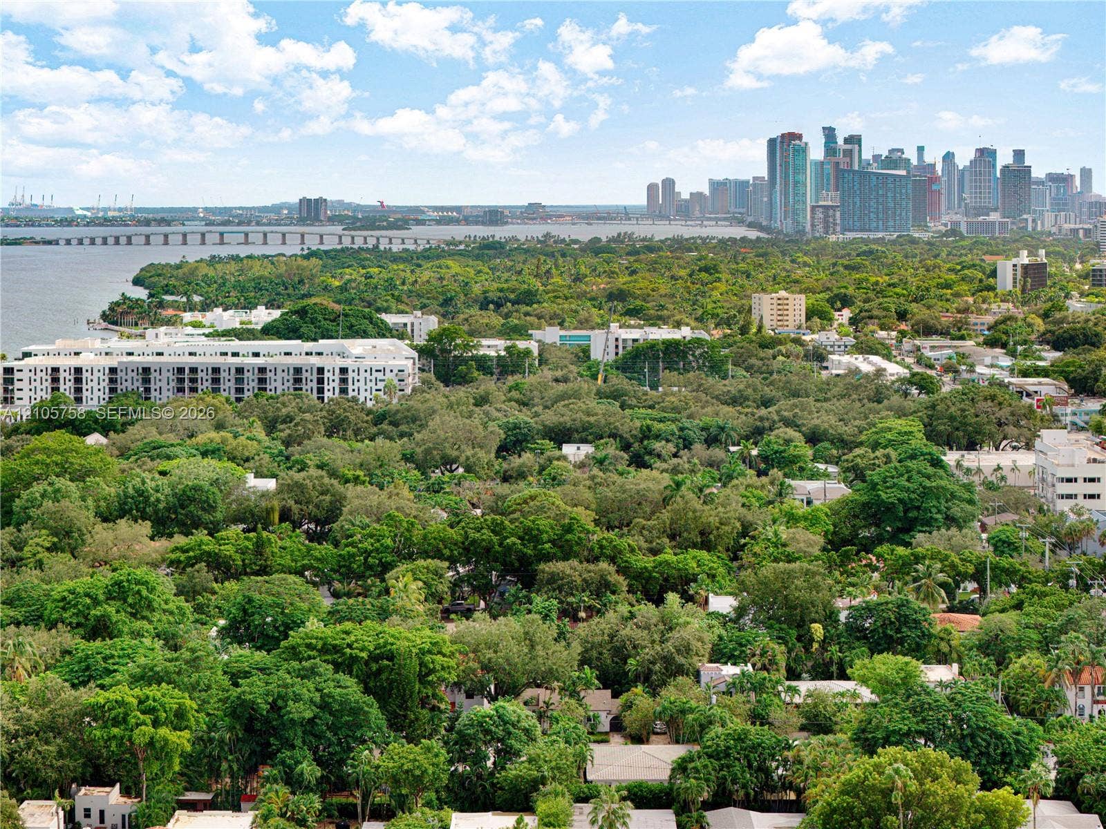 668 NE 70th Street, Miami, FL 33138 Aerial perspective showcasing an expansive tree canopy, waterfront exposure, bridge infrastructure, and distant cityscape skyline