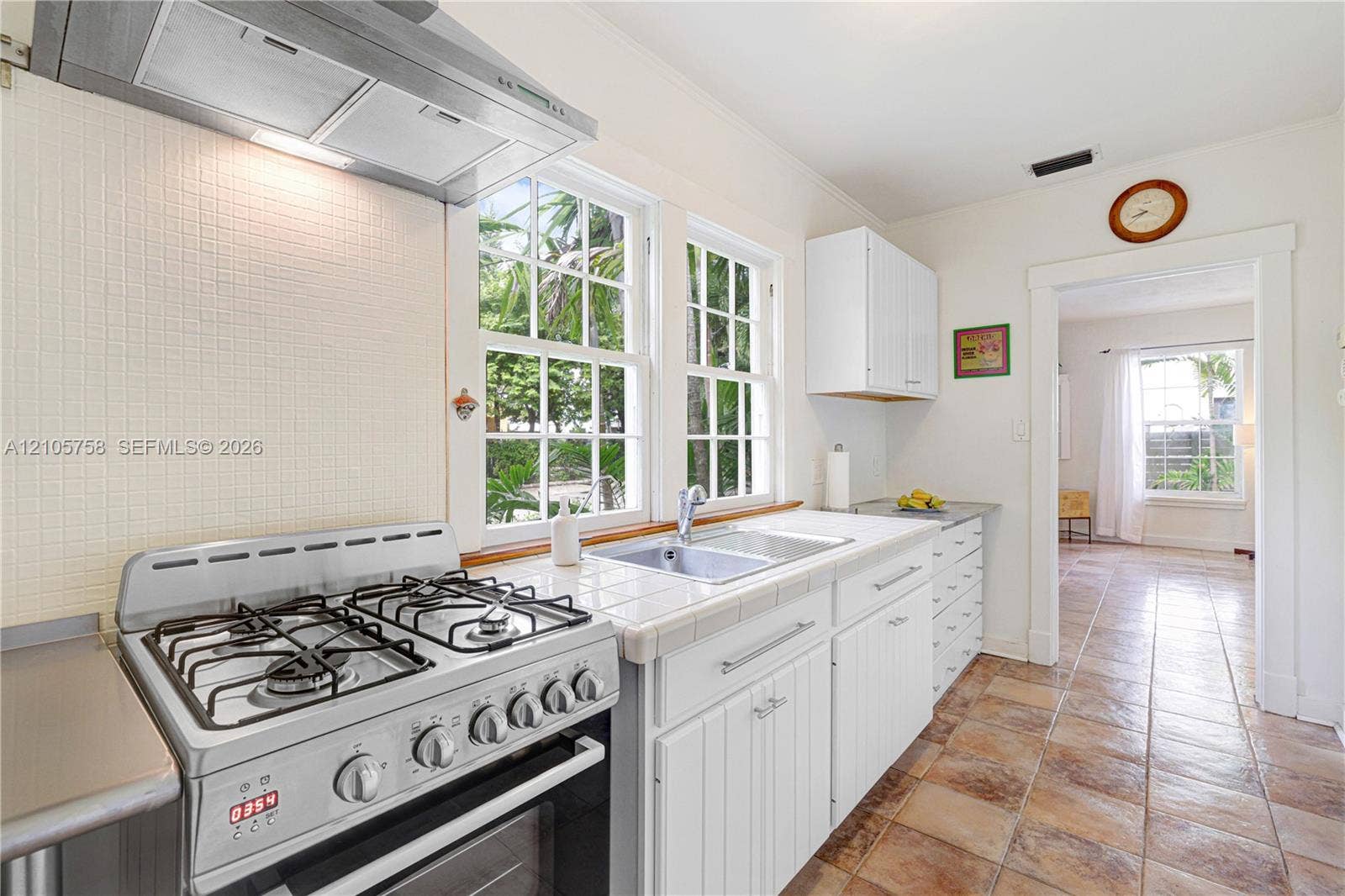668 NE 70th Street, Miami, FL 33138 Kitchen featuring white cabinetry, tiled countertops, stainless steel gas range, stainless steel range hood, and tile flooring