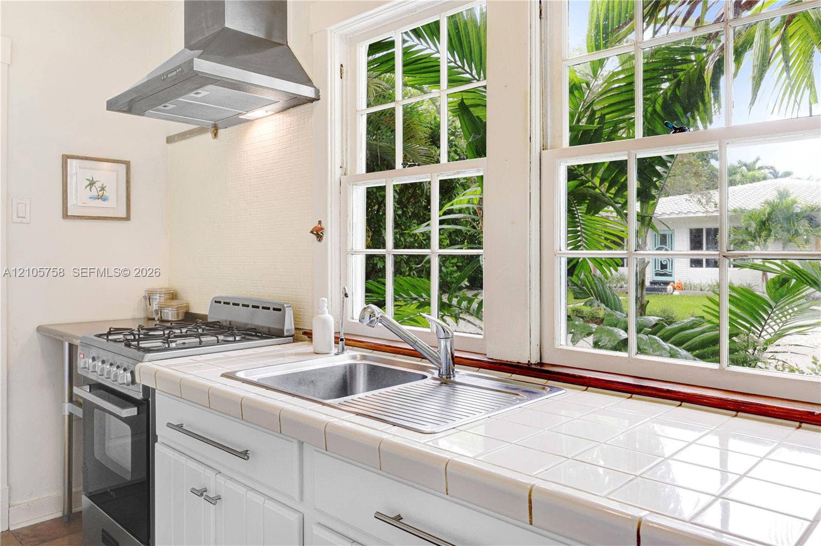 668 NE 70th Street, Miami, FL 33138 Kitchen featuring white tiled countertops, stainless steel dual-basin sink with a goose-neck faucet, freestanding stainless steel gas range, and a stainless steel vent hood