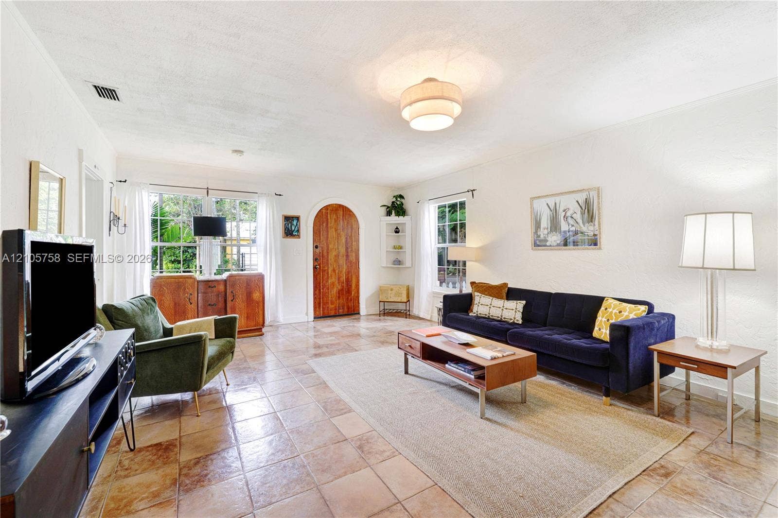 668 NE 70th Street, Miami, FL 33138 Spacious living area featuring square tile flooring, arched wooden entry door, multi-pane windows, and built-in corner shelving