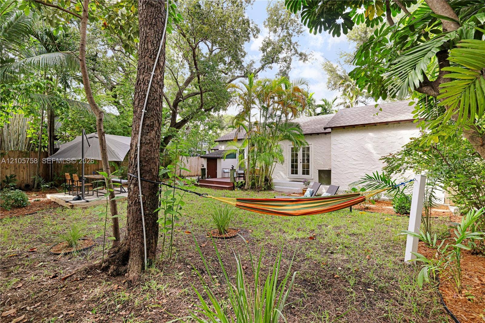 668 NE 70th Street, Miami, FL 33138 Expansive backyard featuring mature trees, wood decking, and white-stucco exterior finish