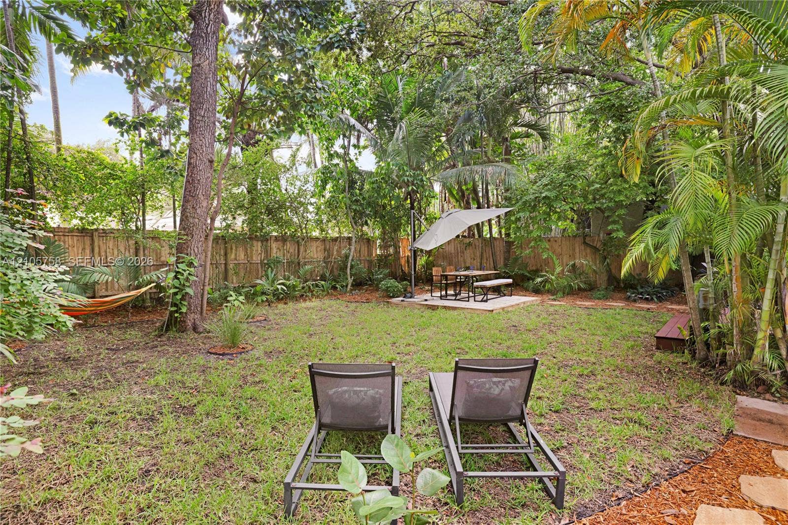 668 NE 70th Street, Miami, FL 33138 Expansive backyard featuring a lush landscape, mature trees, a natural-material privacy fence, and a paved patio area