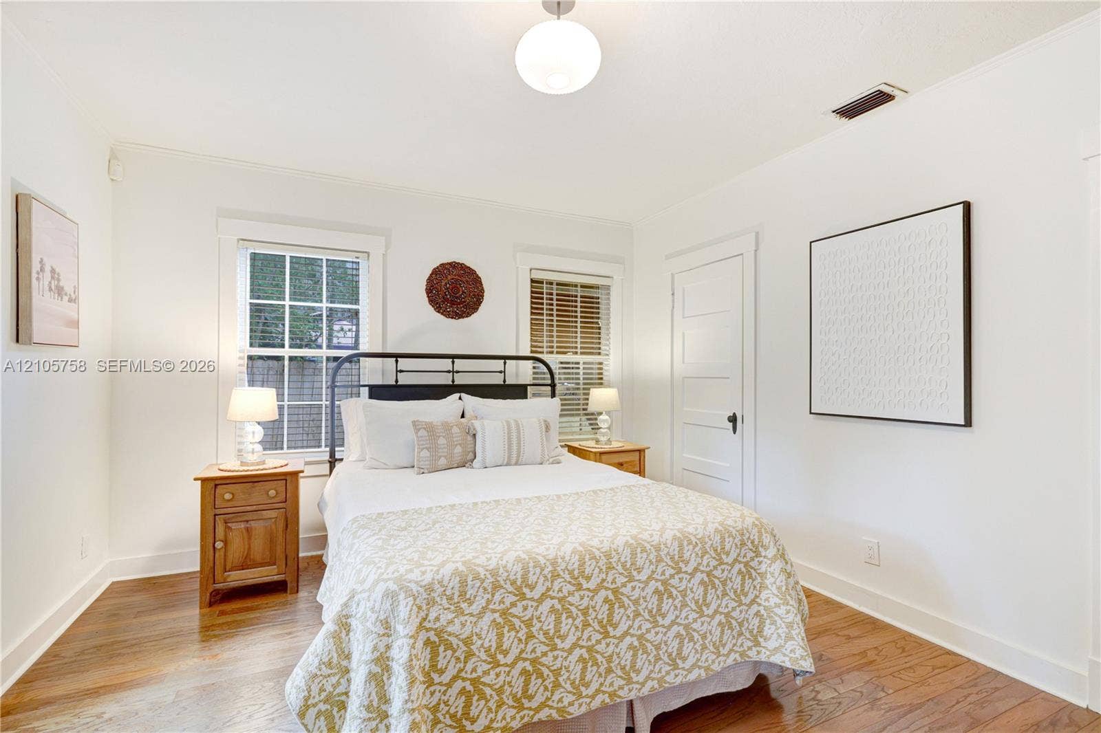 668 NE 70th Street, Miami, FL 33138 Room featuring wood-finish flooring, two double-hung windows with exterior grid muntins, a white-paneled interior door, and a spherical pendant light fixture