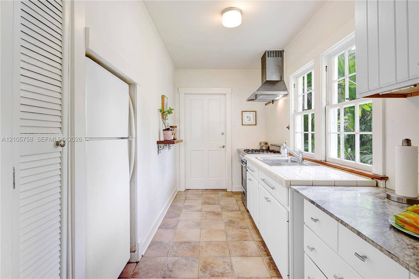 668 NE 70th Street, Miami, FL 33138 Kitchen featuring white shaker-style cabinetry, a stainless steel range hood, stone-finish countertops, tile flooring, and dual-sash windows
