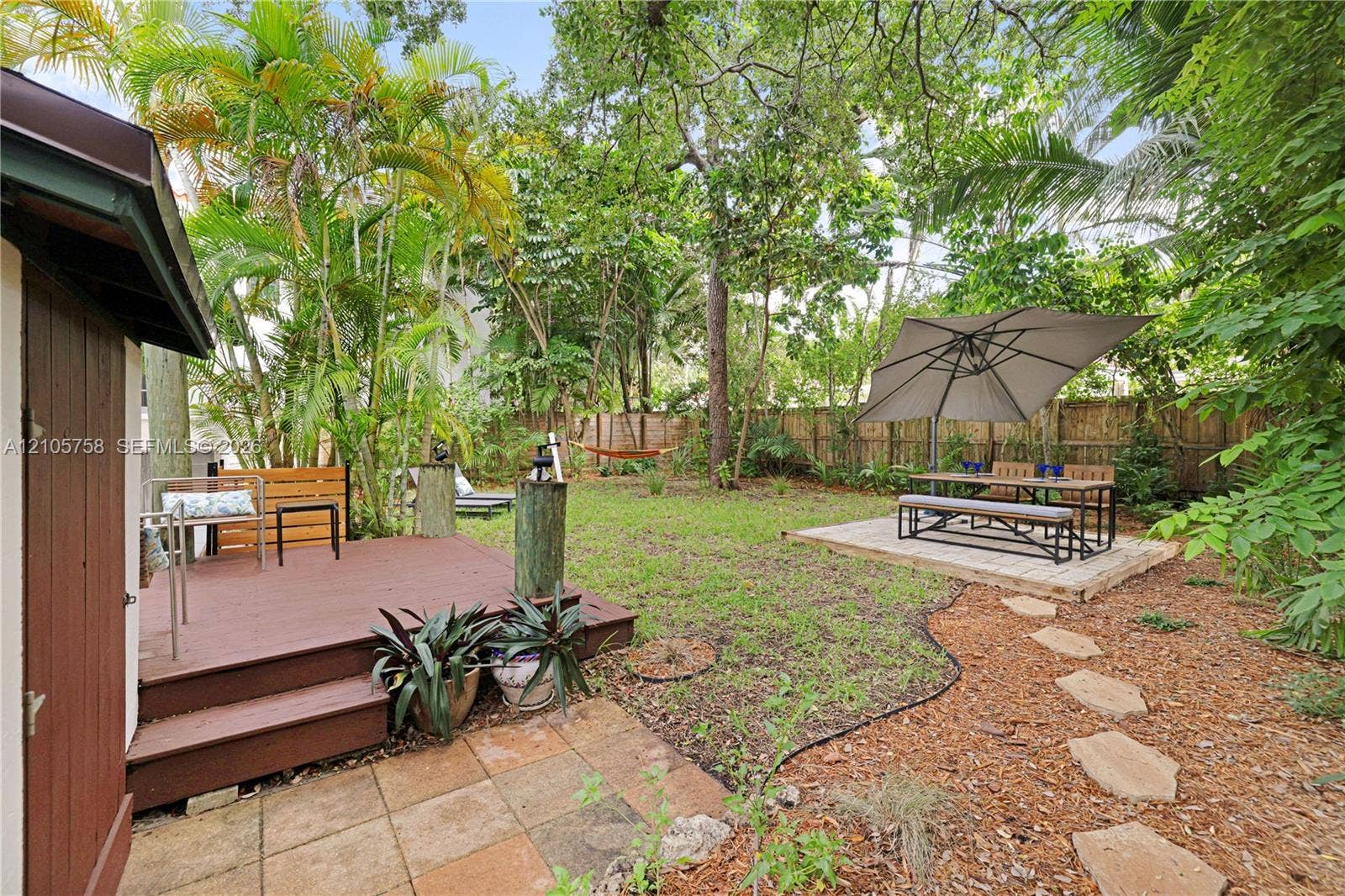 668 NE 70th Street, Miami, FL 33138 Private backyard featuring a wooden deck, stone paver patio, stone-path walkway, wood-plank fencing, and mature trees