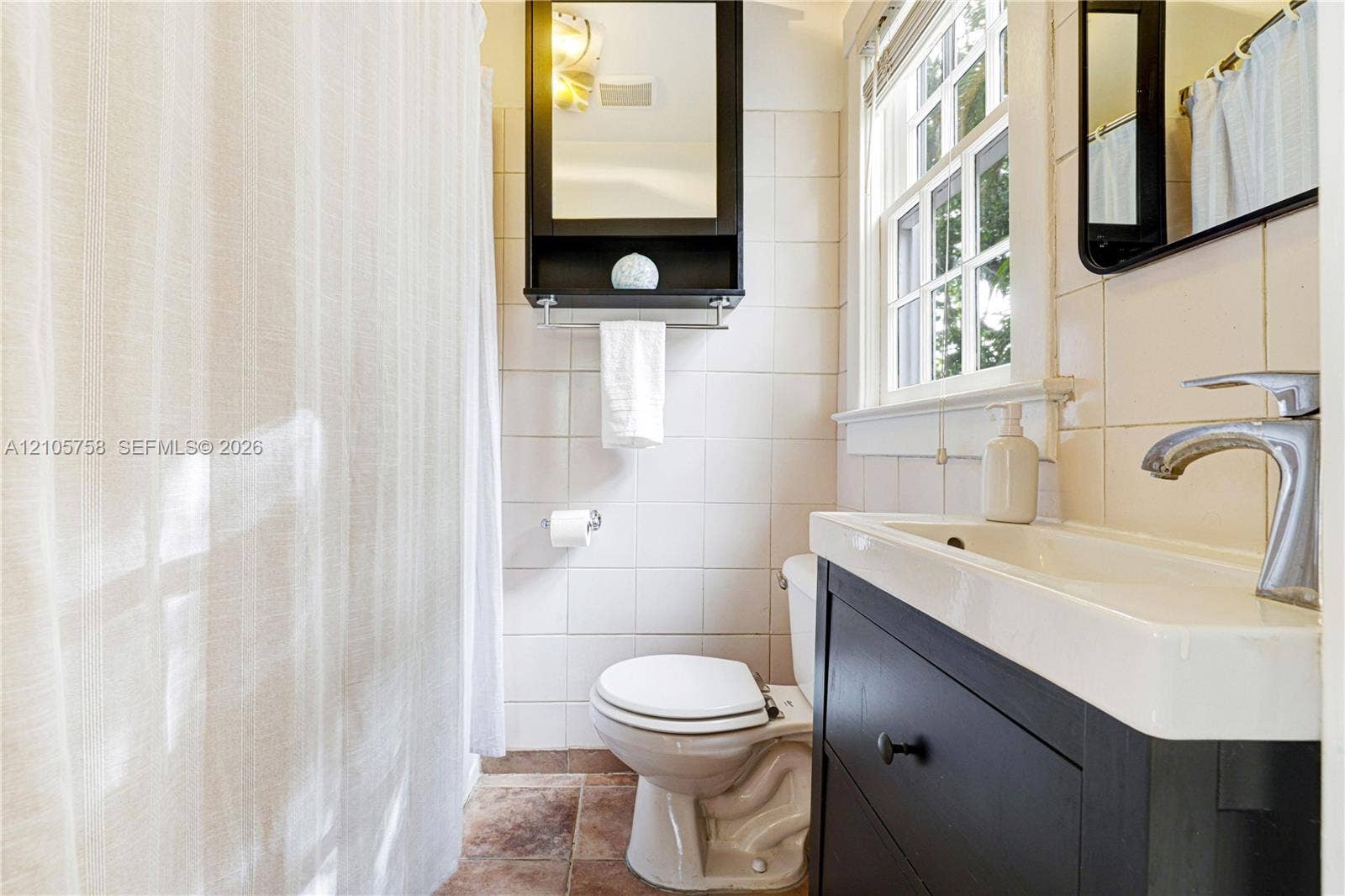 668 NE 70th Street, Miami, FL 33138 Bathroom featuring a dark wood-finish vanity with an integrated rectangular basin, a wall-mounted mirrored medicine cabinet, square wall tiling, and a window with divided lites