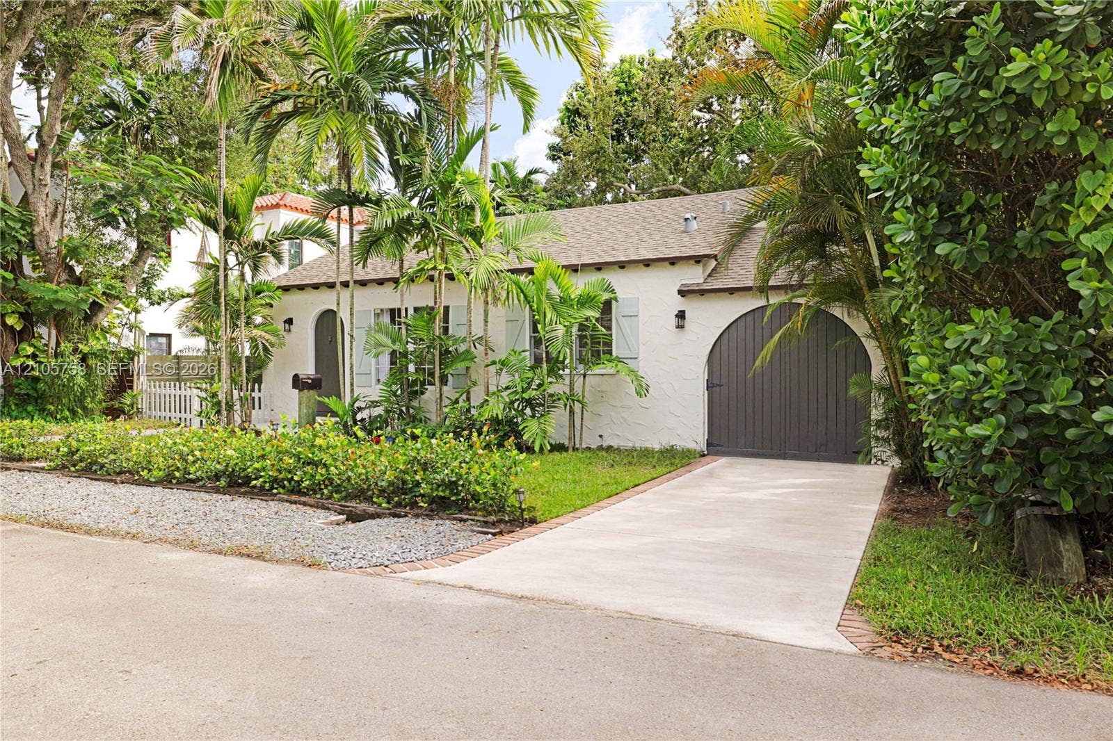 668 NE 70th Street, Miami, FL 33138 Single-story residence featuring a textured stucco exterior, arched front entryway, arched garage door, shuttered windows, and a concrete driveway